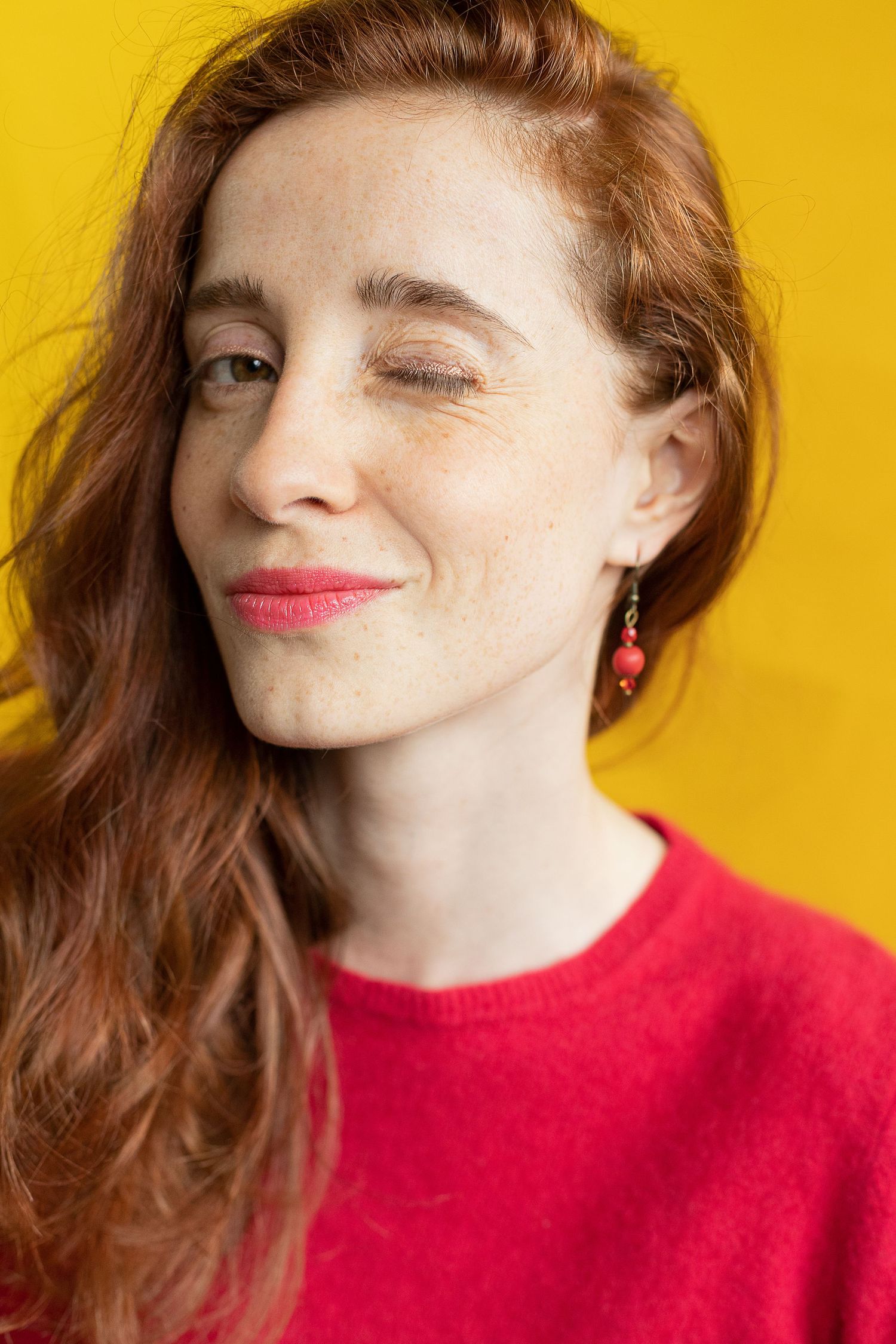 Portrait studio sur fond jaune d'une femme rousse faisant un clin d'oeil