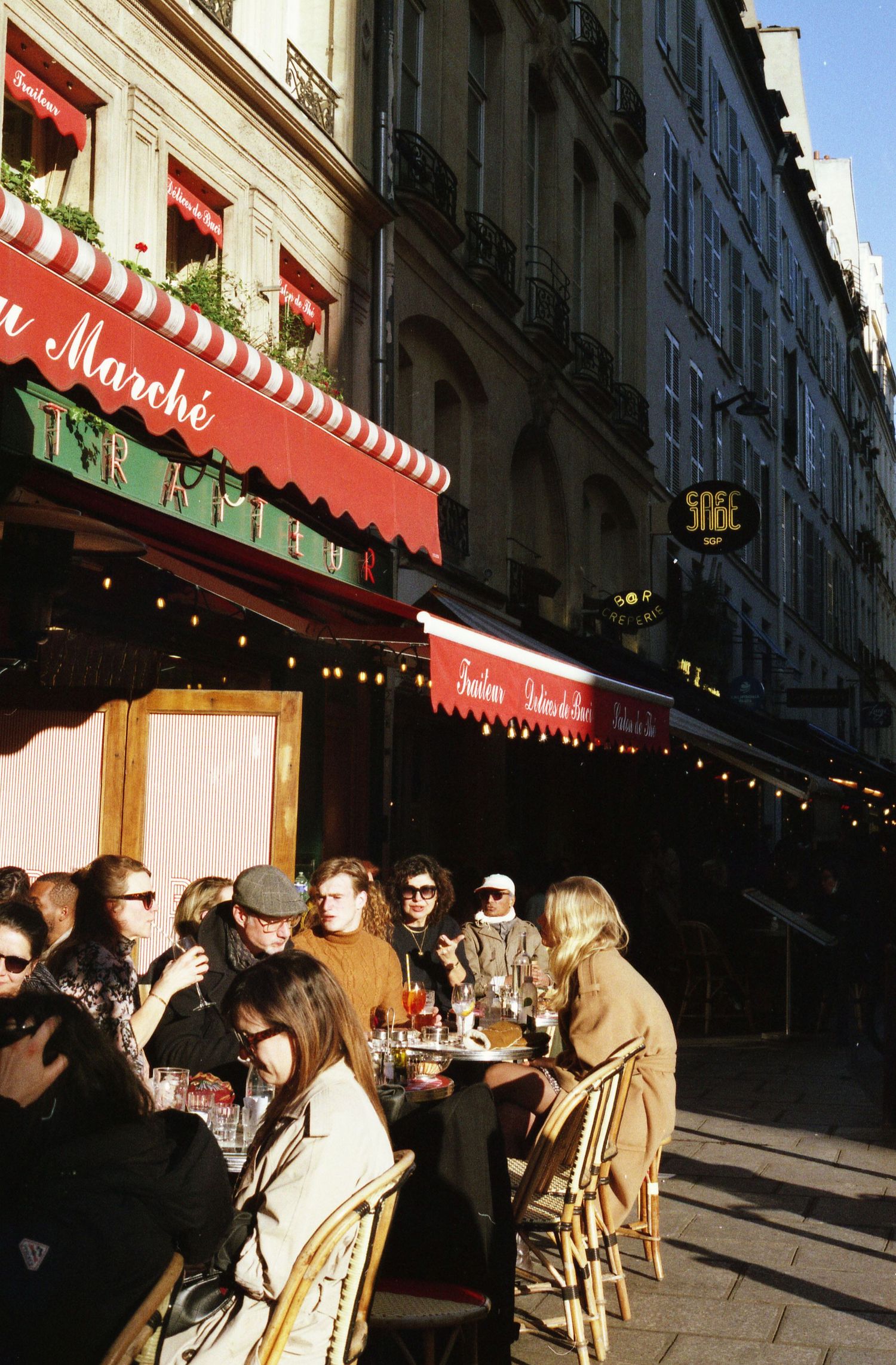 Photo argentique prise à Paris de personnes installées en terrasse. La terrasse est ensoleillée.