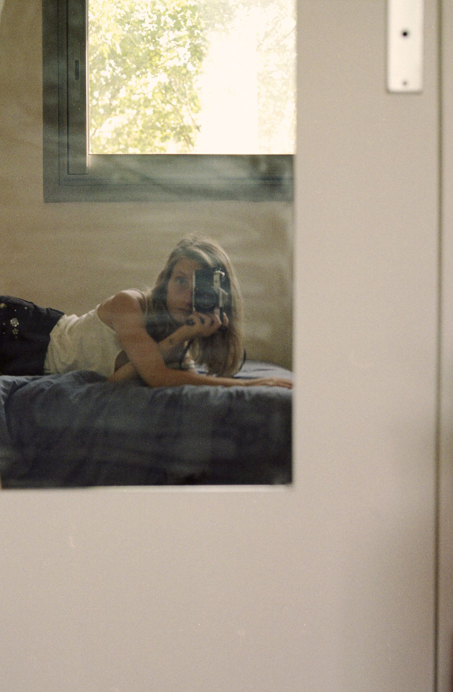 Autoportrait argentique d'une femme allongée pris face au miroir, une fenêtre en arrière plan