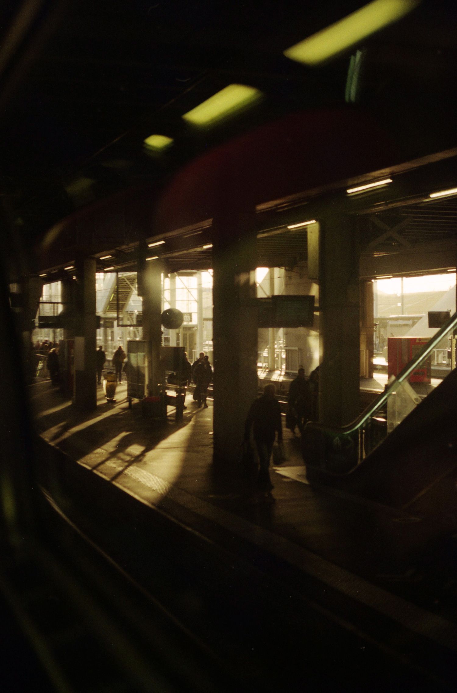 Photo argentique prise à travers la vitre de la fenêtre d'un train. On y voit la gare de Renne illuminée par le soleil qui se lève.
