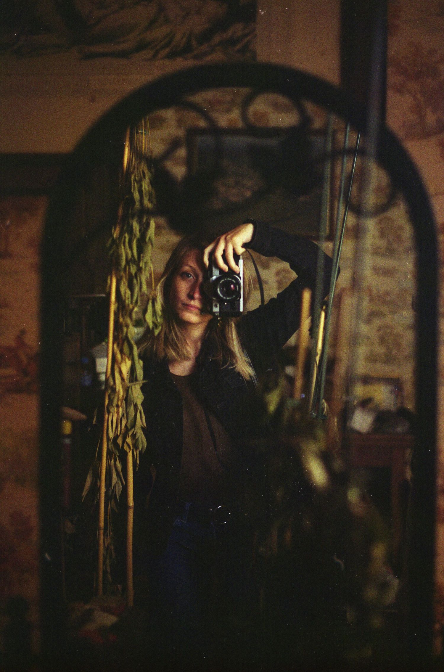 Autoportrait argentique d'une femme, pris dans un miroir en fer orné. Papier peint vintage sur les murs.