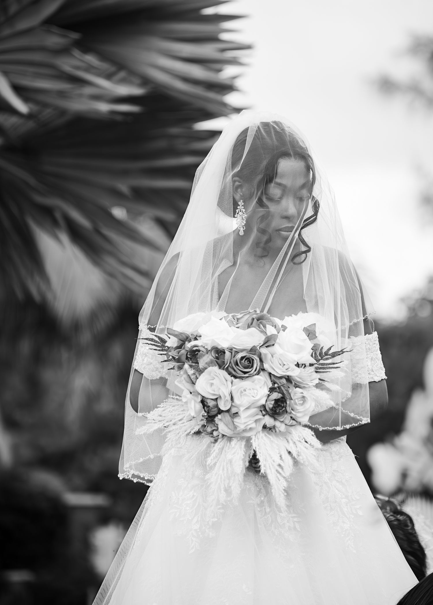 A black and white wedding photo showcasing a bride in a veil holding an elegant bouquet of roses in a garden setting.