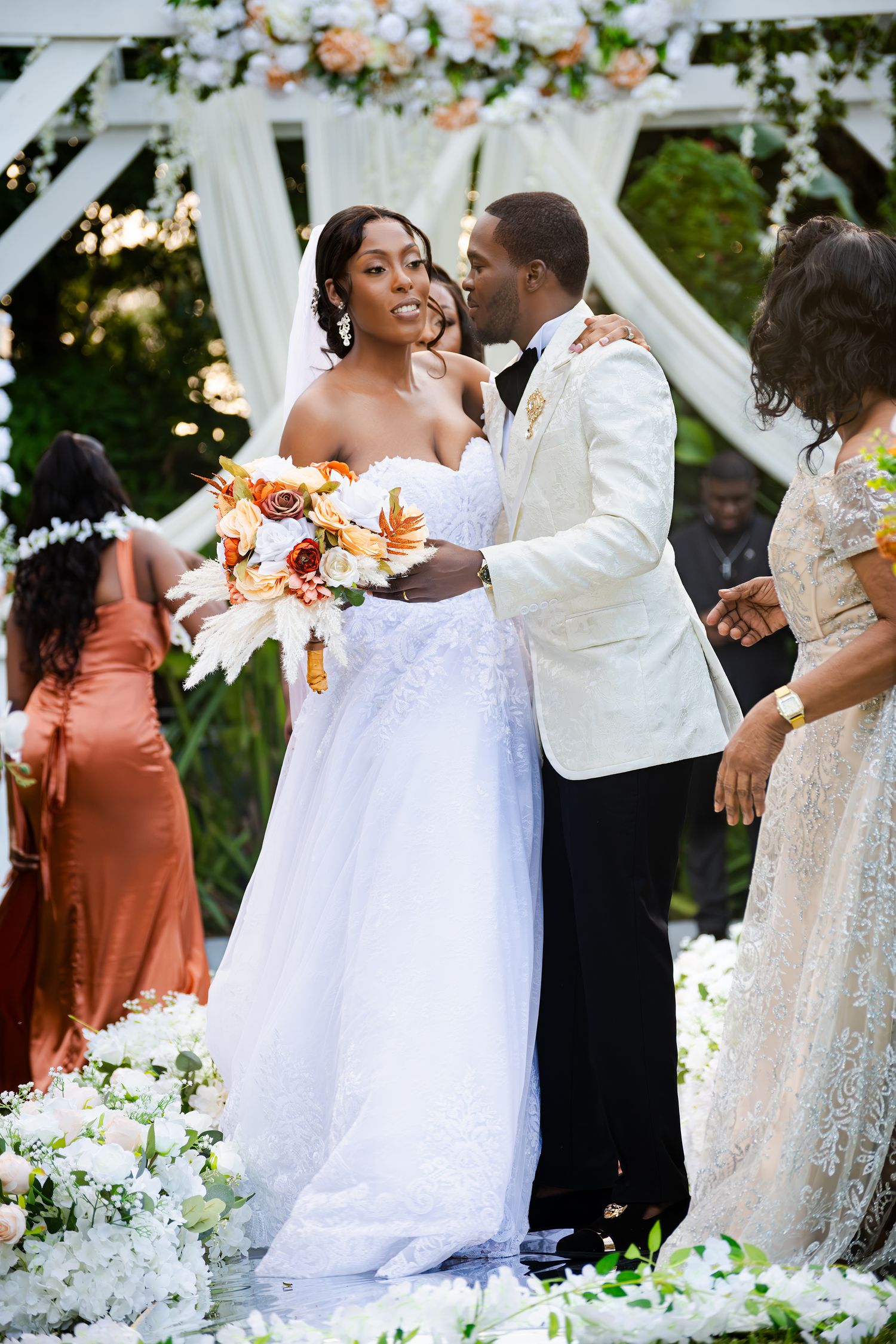 Wedding celebration outdoors with floral arch and couple in white formal attire.