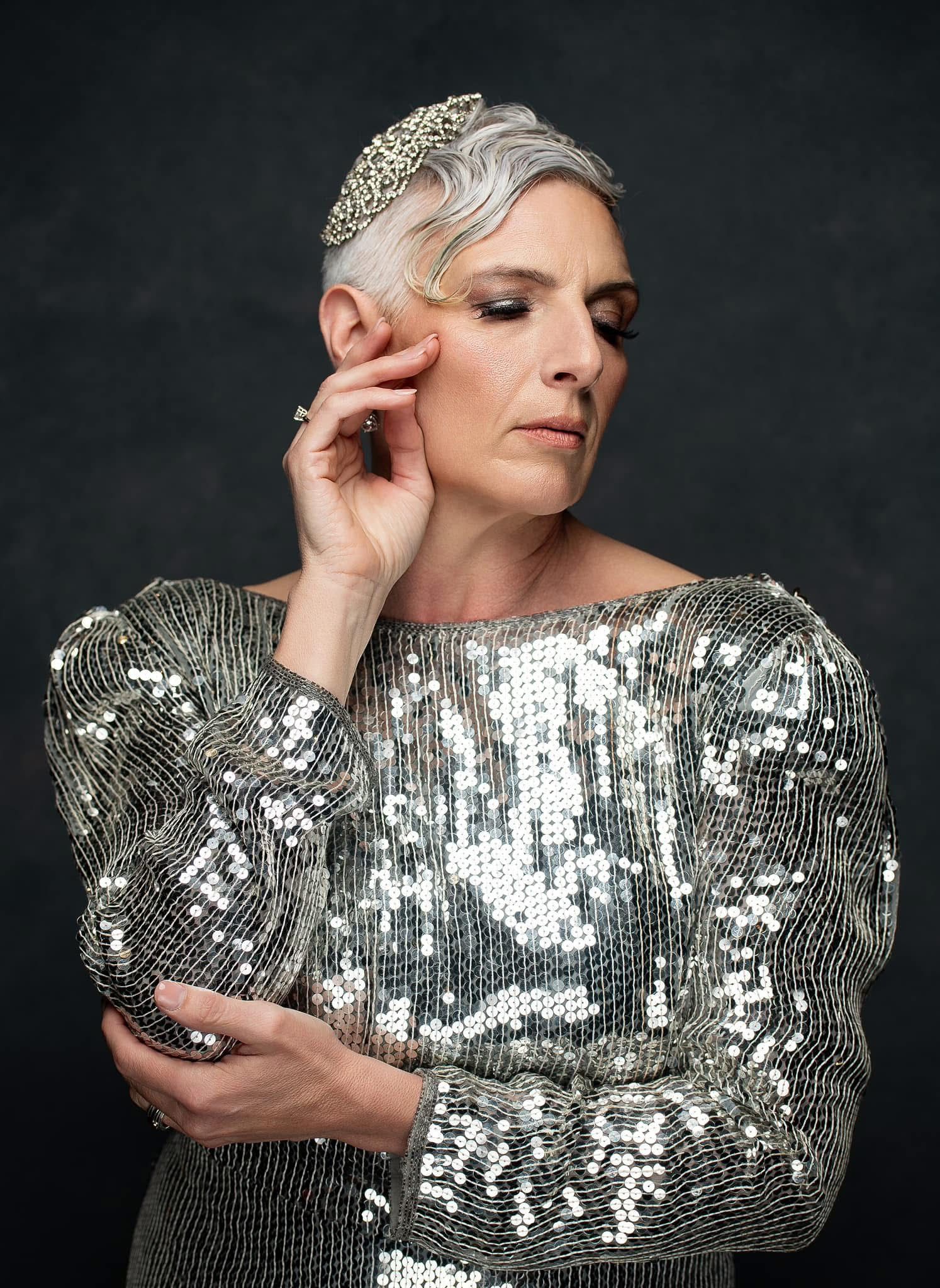 A dramatic studio portrait showing a silver sequined dress and crystal headpiece against a dark background.