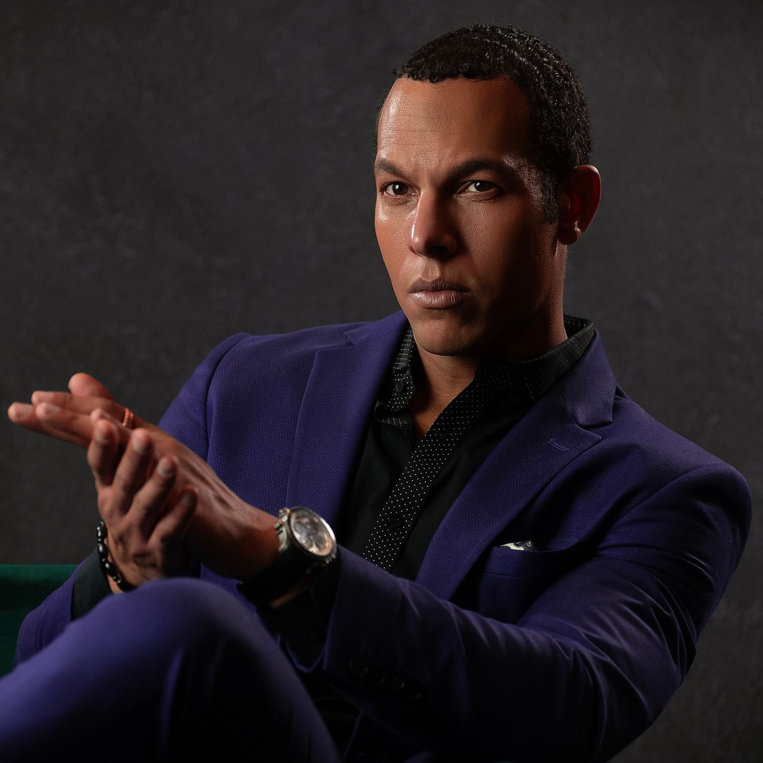 Professional portrait of person in navy blue suit jacket seated against dark background.