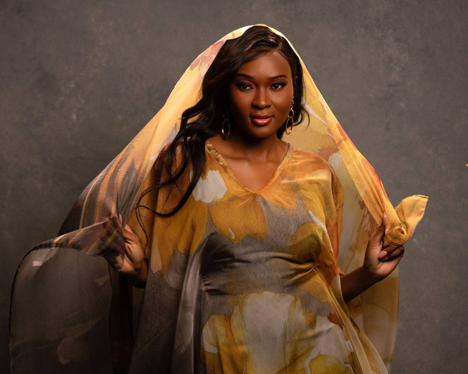 A dramatic portrait featuring flowing golden fabric and soft lighting against a textured background.