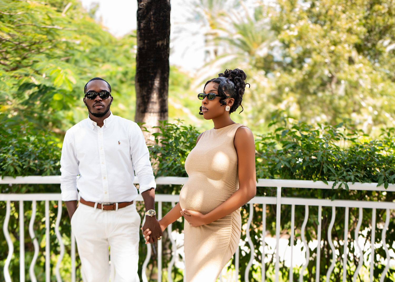 Maternity photo of couple in white outfits standing on outdoor balcony.