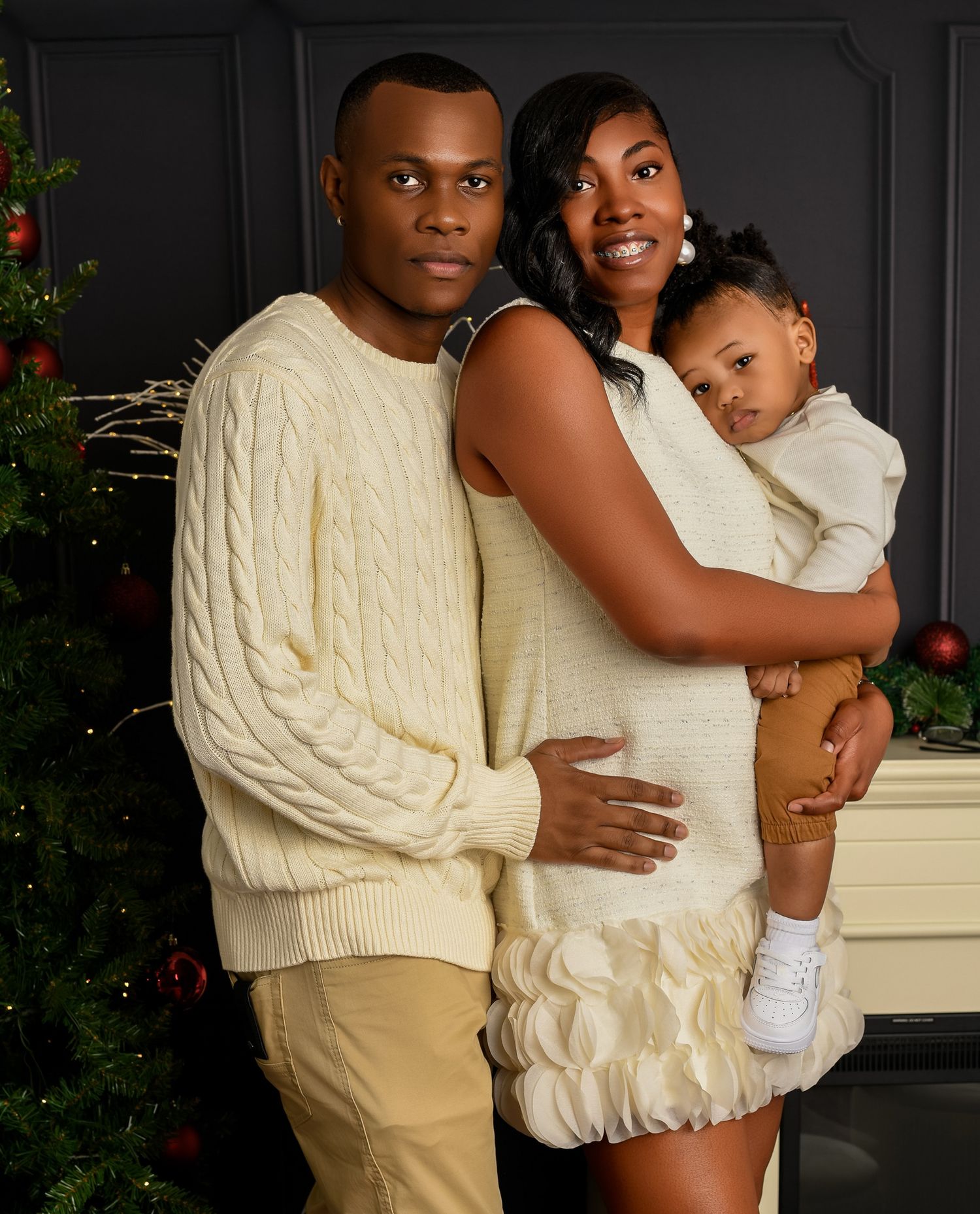 A family in cream-colored outfits poses together by their Christmas tree.