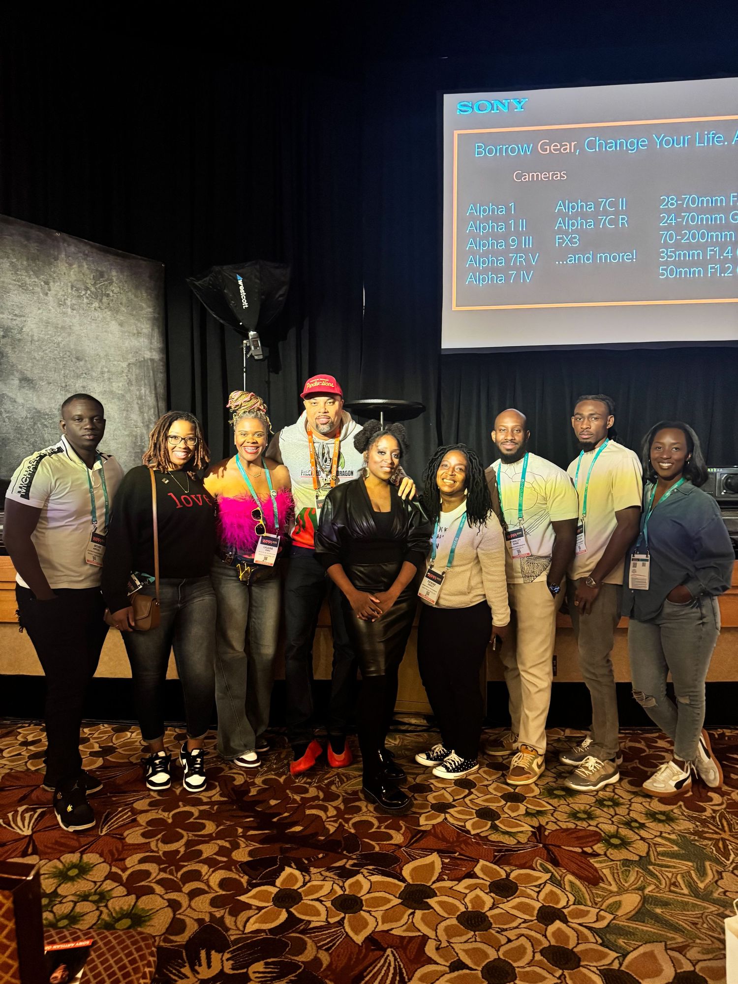 Team members pose together at conference with projection screen visible in background.