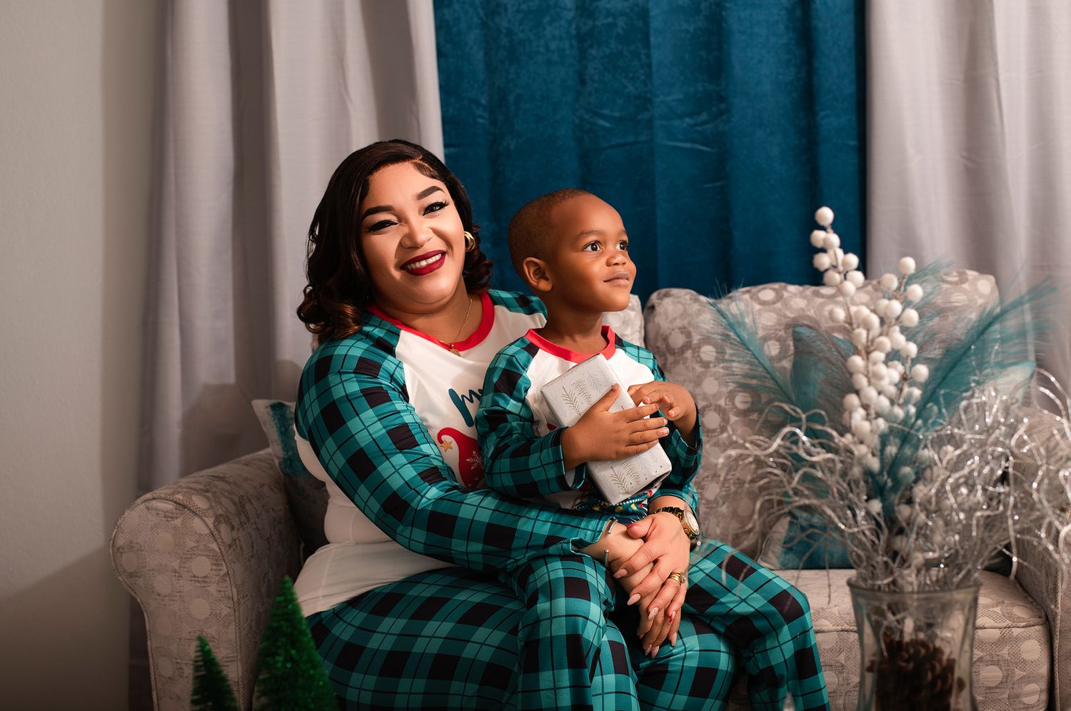 A pair wearing matching plaid pajamas share a festive holiday moment on a couch.