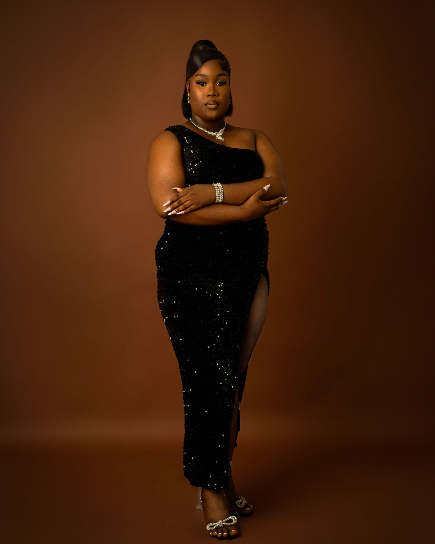 An elegant figure in a black sequined gown poses confidently against a warm brown background.