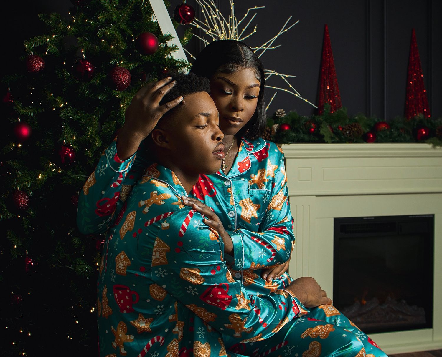 Two people in blue floral pajamas pose in front of a Christmas tree and fireplace.