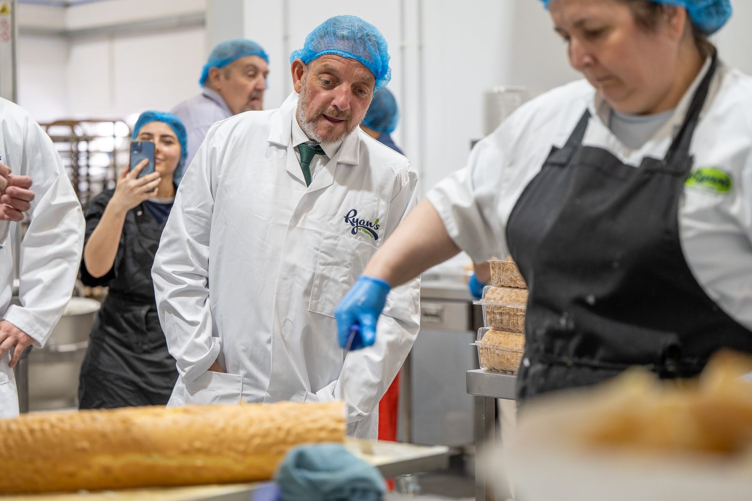 Food production workers in protective gear inspecting fresh baked goods on assembly line.