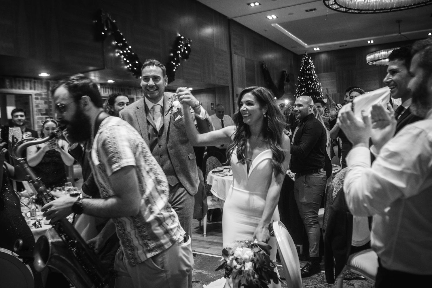 Wedding guests dancing and celebrating on a lively dance floor with holiday decorations visible.