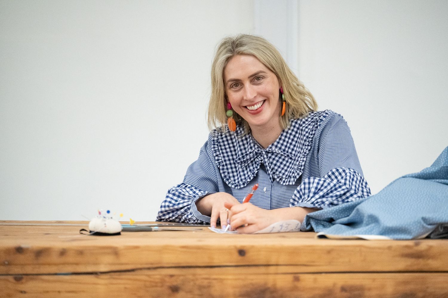 Person in blue checkered shirt working at rustic wooden desk in natural light.