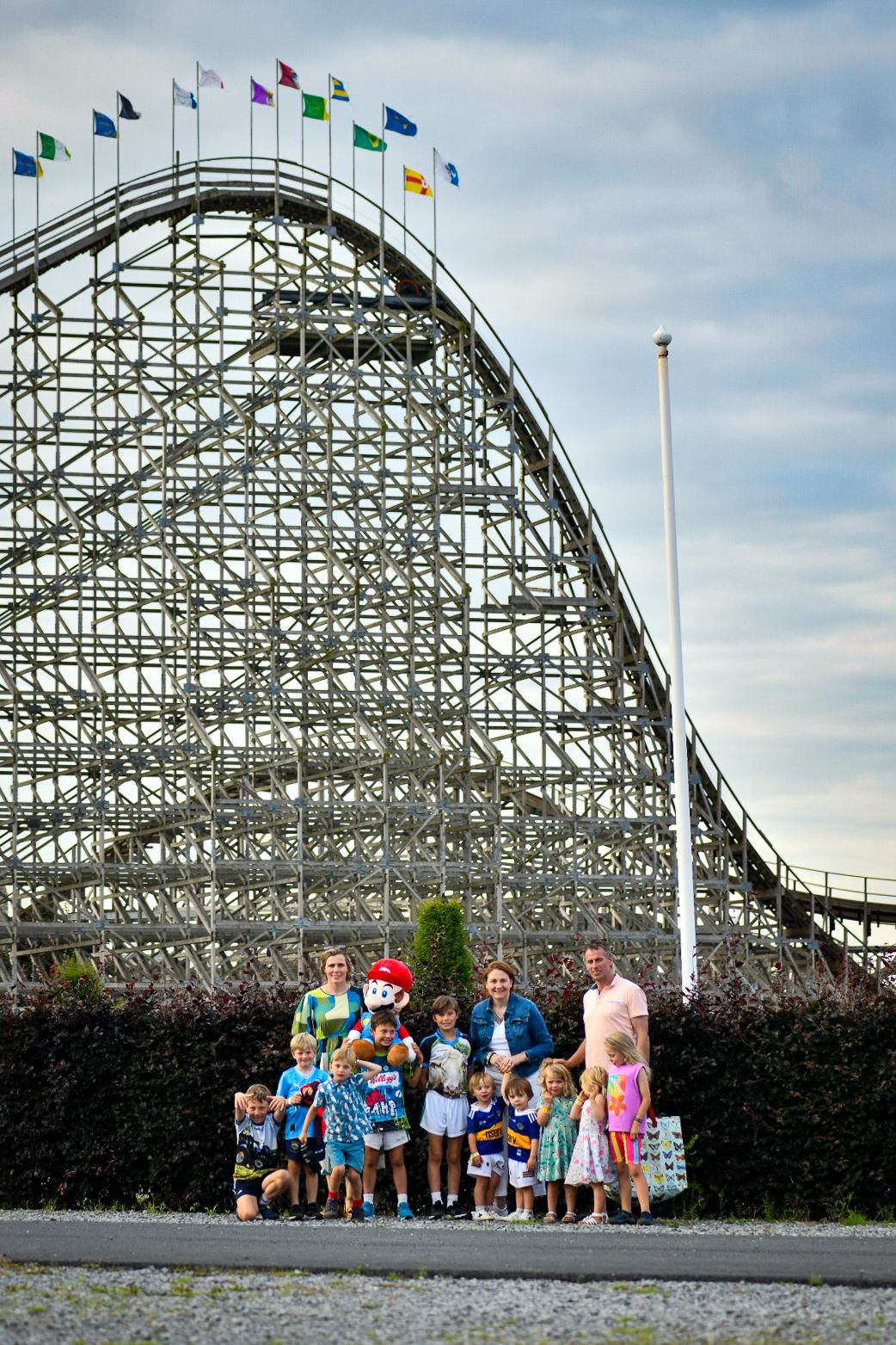 Group photo in front of a large wooden roller coaster with colorful flags waving above.