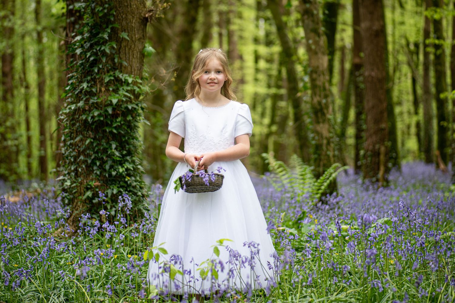 Person in white dress walking through a magical forest filled with purple bluebells.