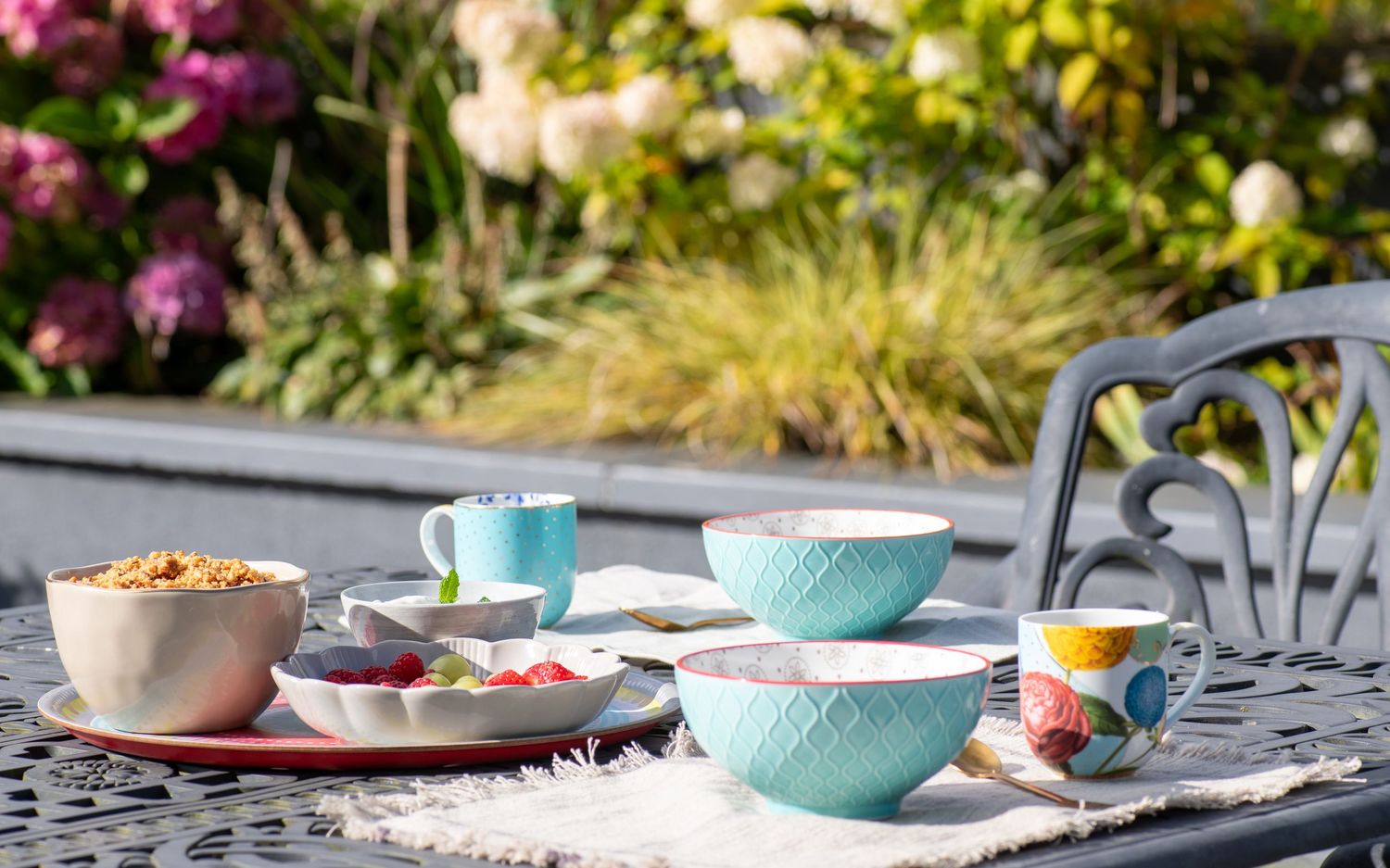 Colorful table setting featuring pink flowers, turquoise plates, and rustic outdoor dining decor.