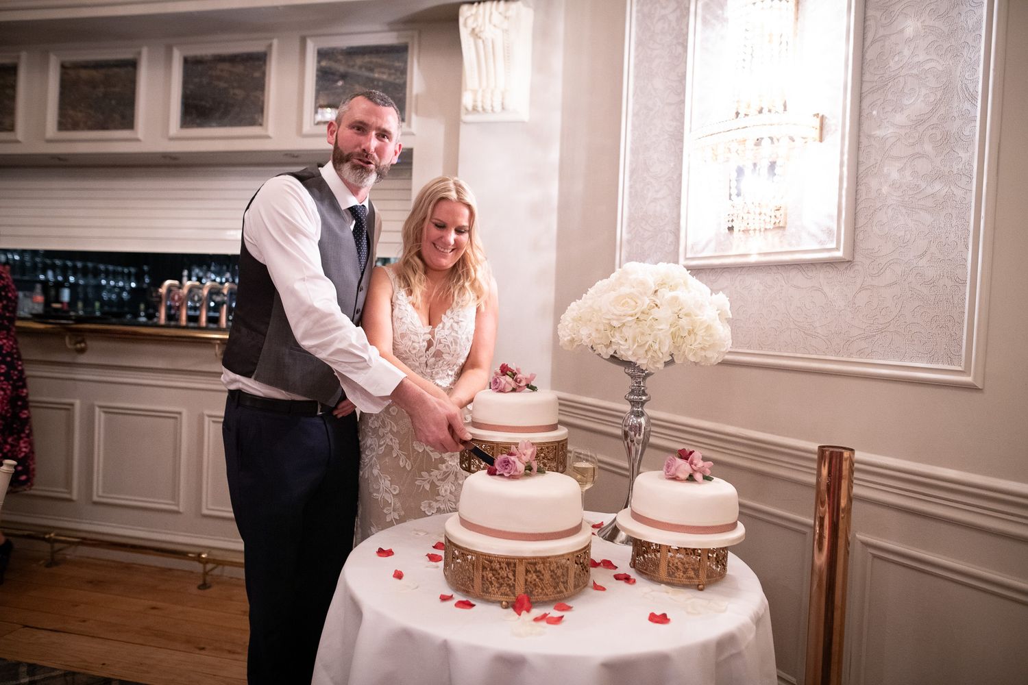 A couple cuts their multi-tiered wedding cake decorated with white flowers at their reception.
