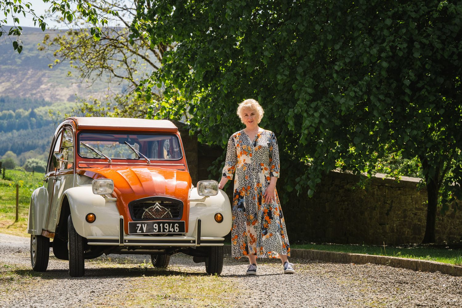 Vintage cars parked on gravel driveway near stone buildings and trees.