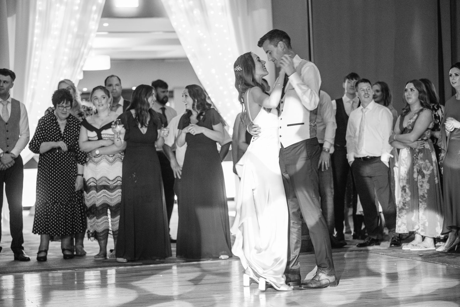 A couple shares an intimate dance moment under spotlight while guests watch from the sidelines.