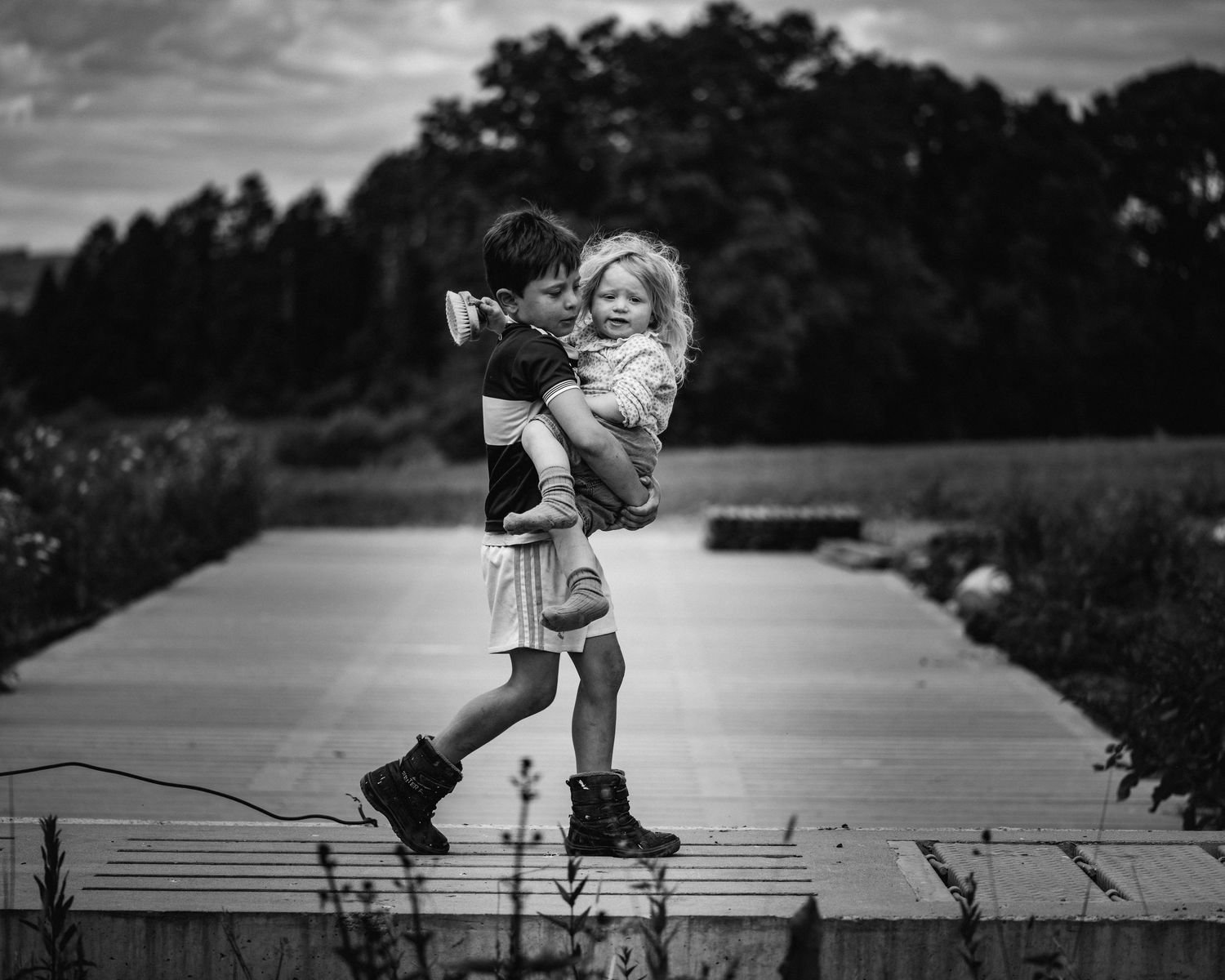 Black and white image capturing playful movement on a pathway with trees in background.