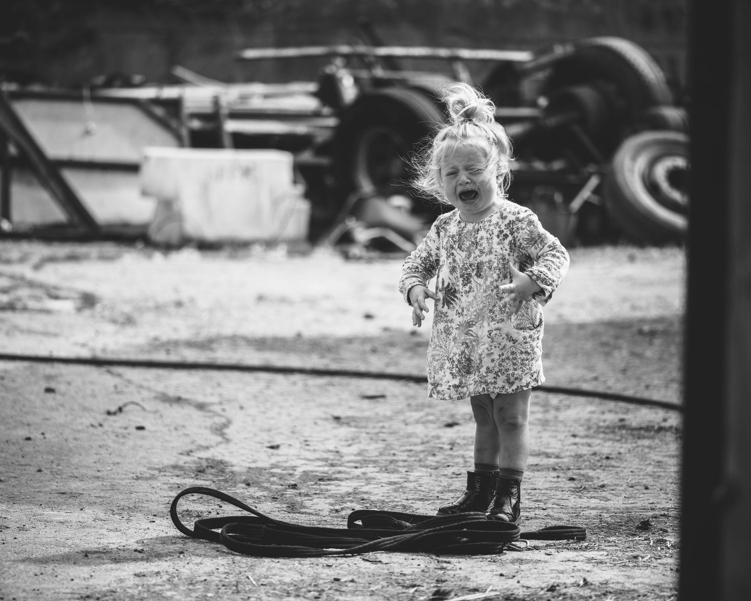 Black and white image of rubber boots and farm equipment in a rustic setting.
