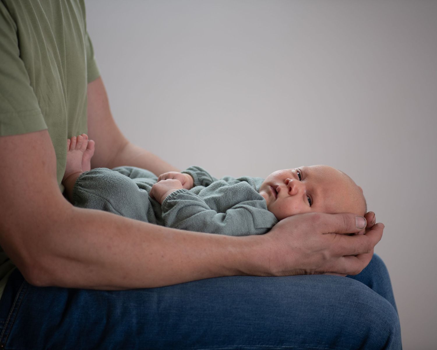 A small infant in blue sleepwear rests on someone's lap against a neutral background.