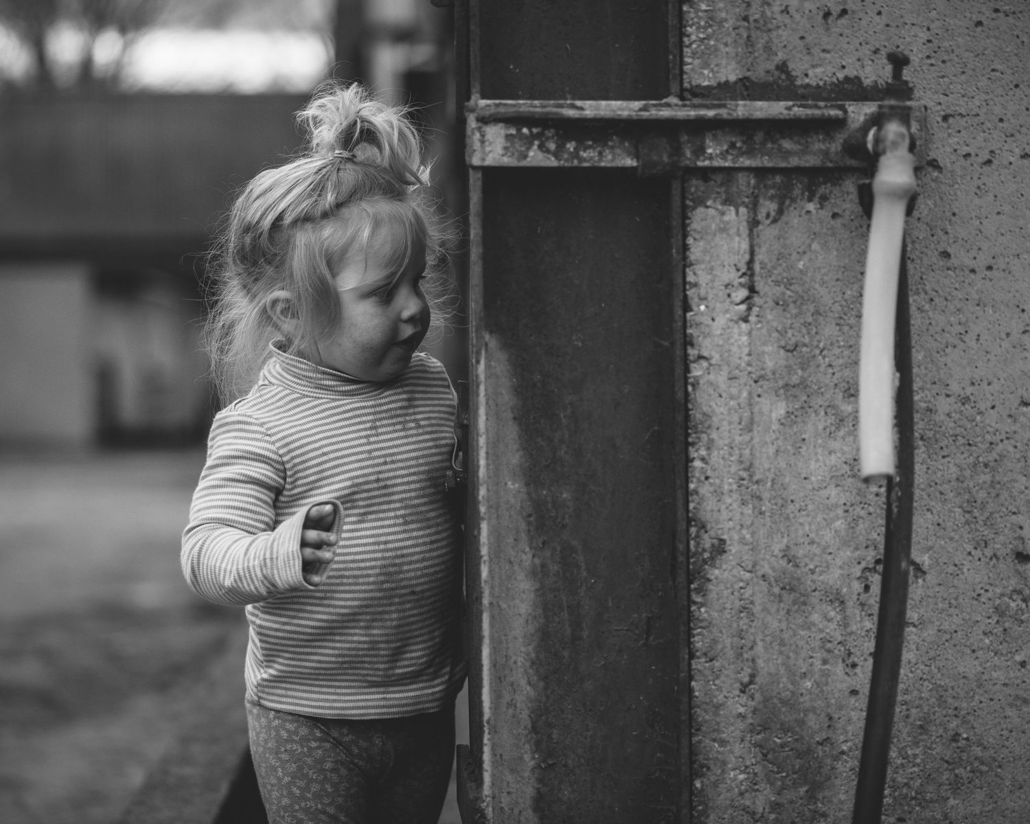 Small figure in striped sweater examining something near a wall outdoors.