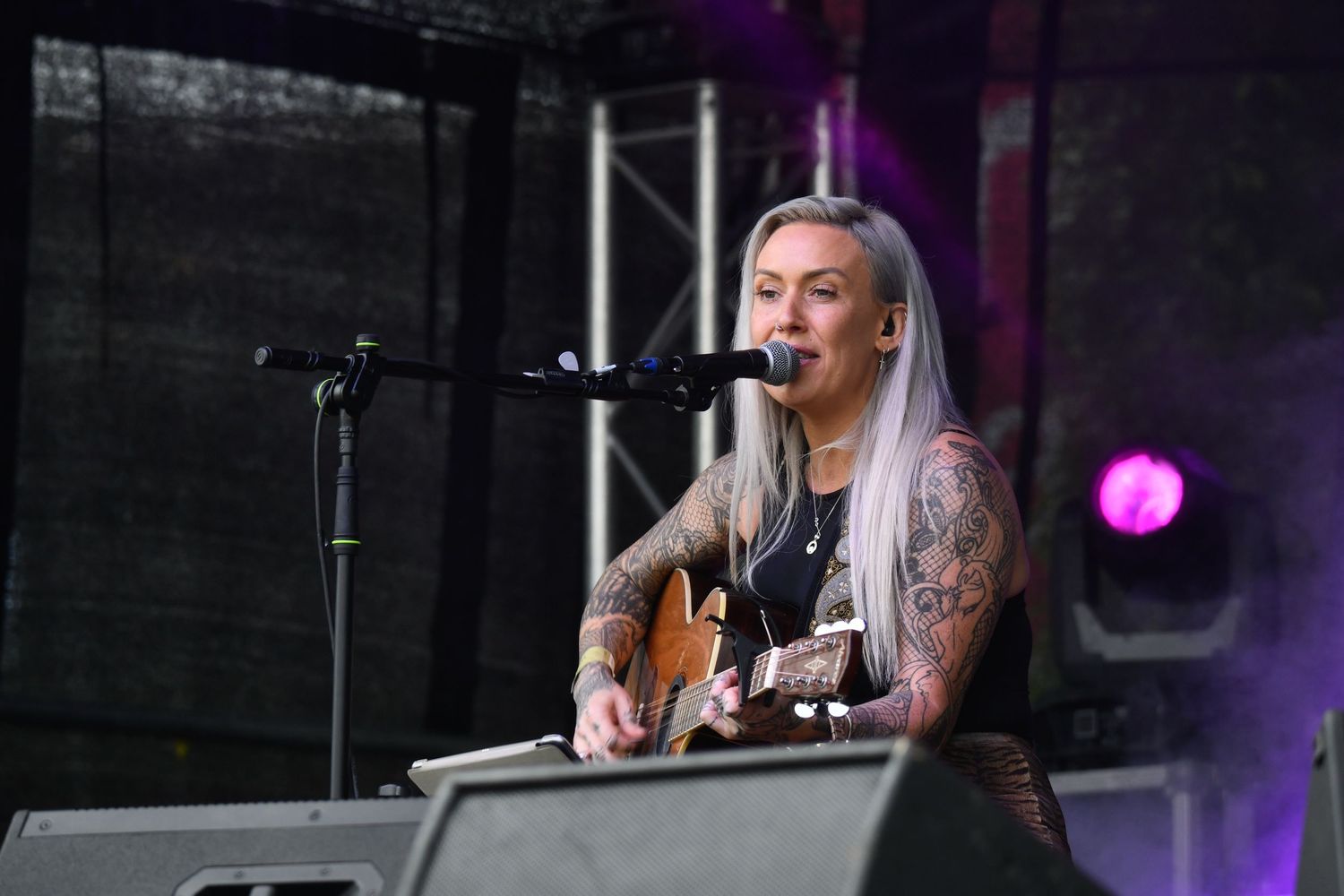 A musician performs with an acoustic guitar on stage with purple lighting effects.