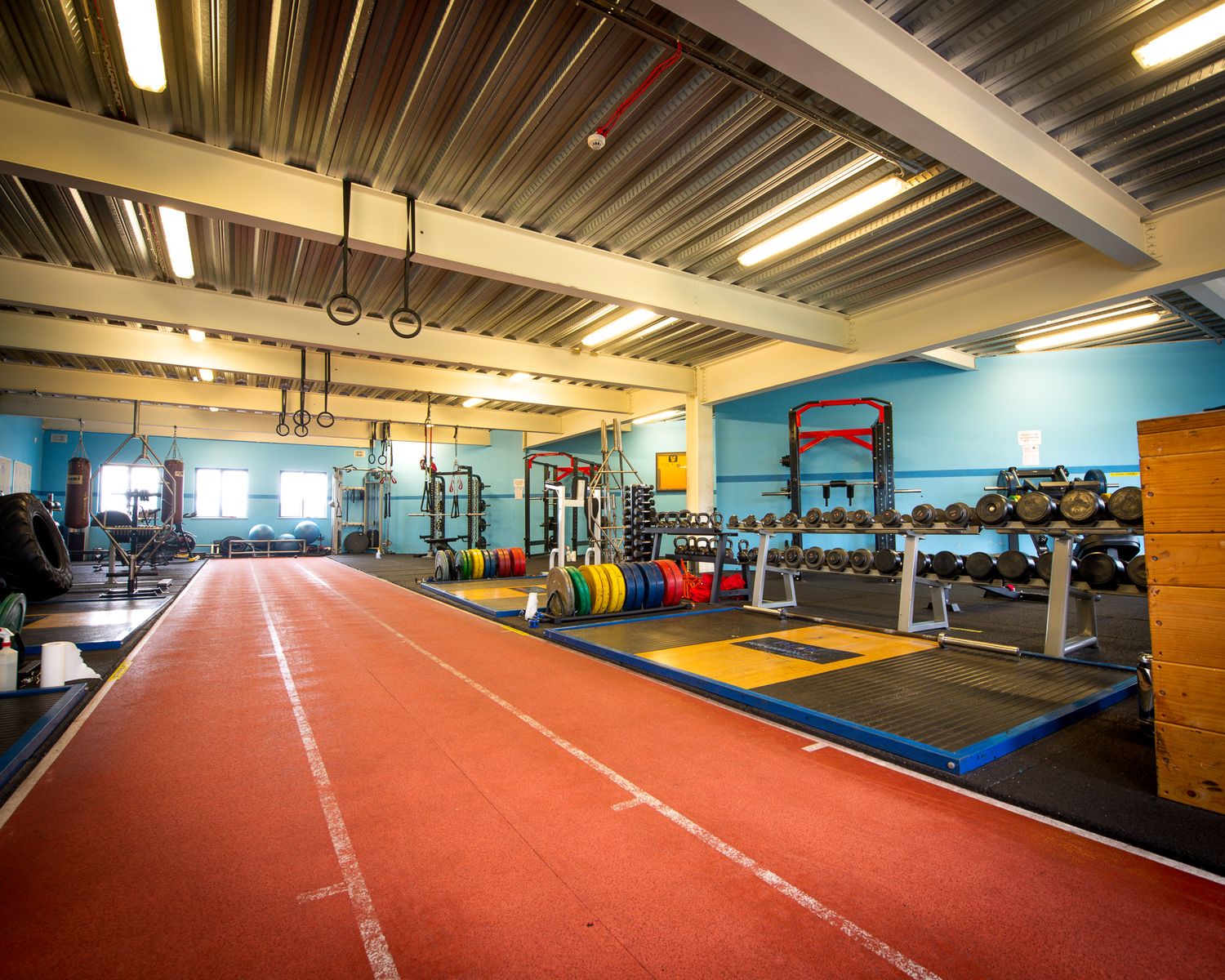Indoor athletic facility featuring a bright red running track and functional fitness training area.