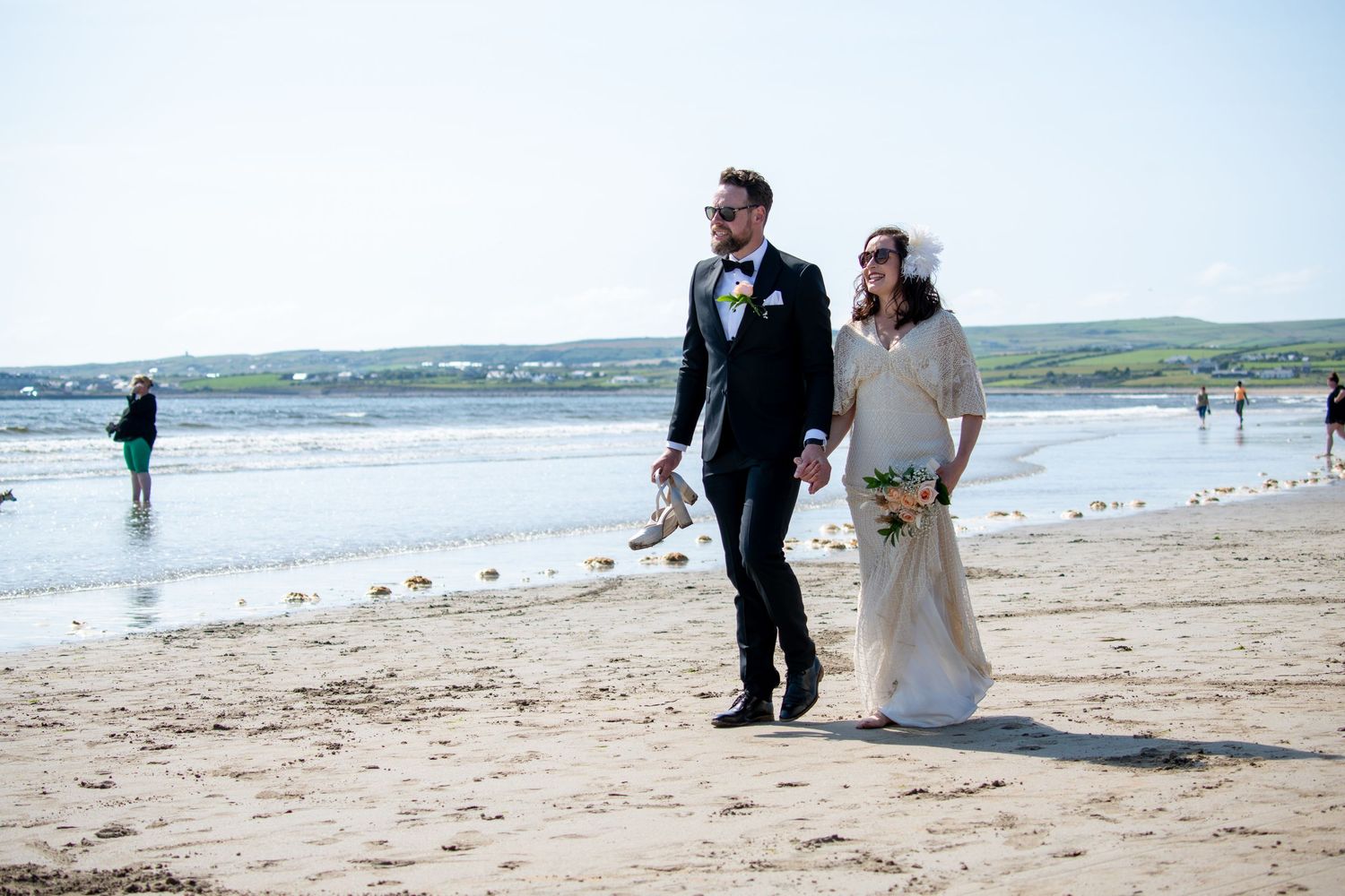 A wedding couple walking along a scenic beach with rolling hills in the background.