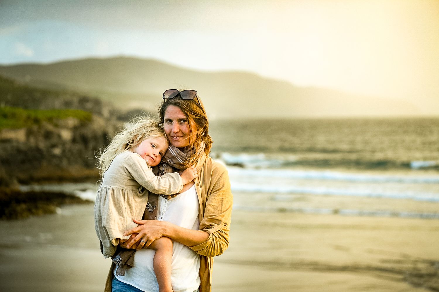 Intimate moment captured at sunset on a rocky beach with mountains in the background.