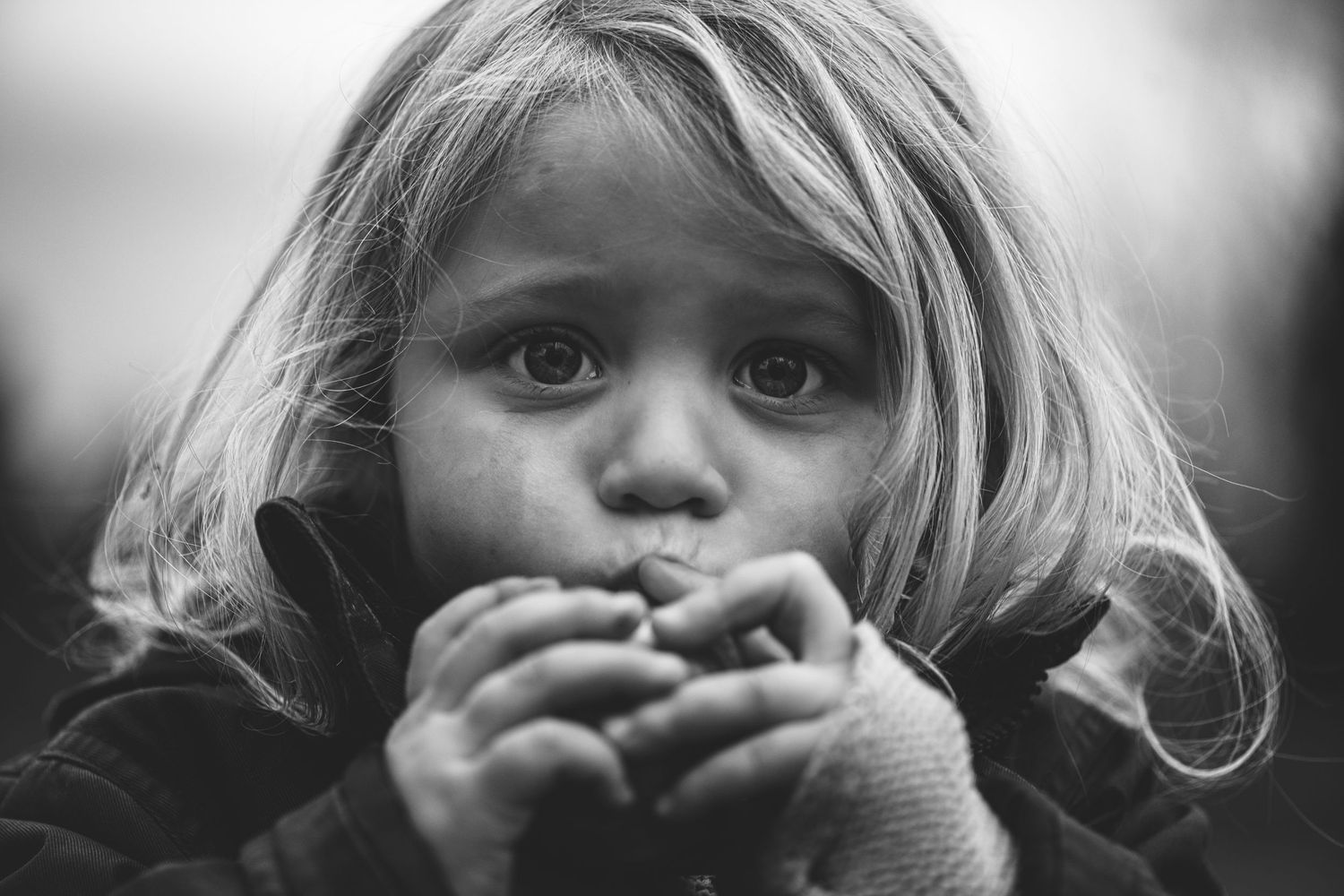 Close-up black and white portrait of small child holding something to their mouth.