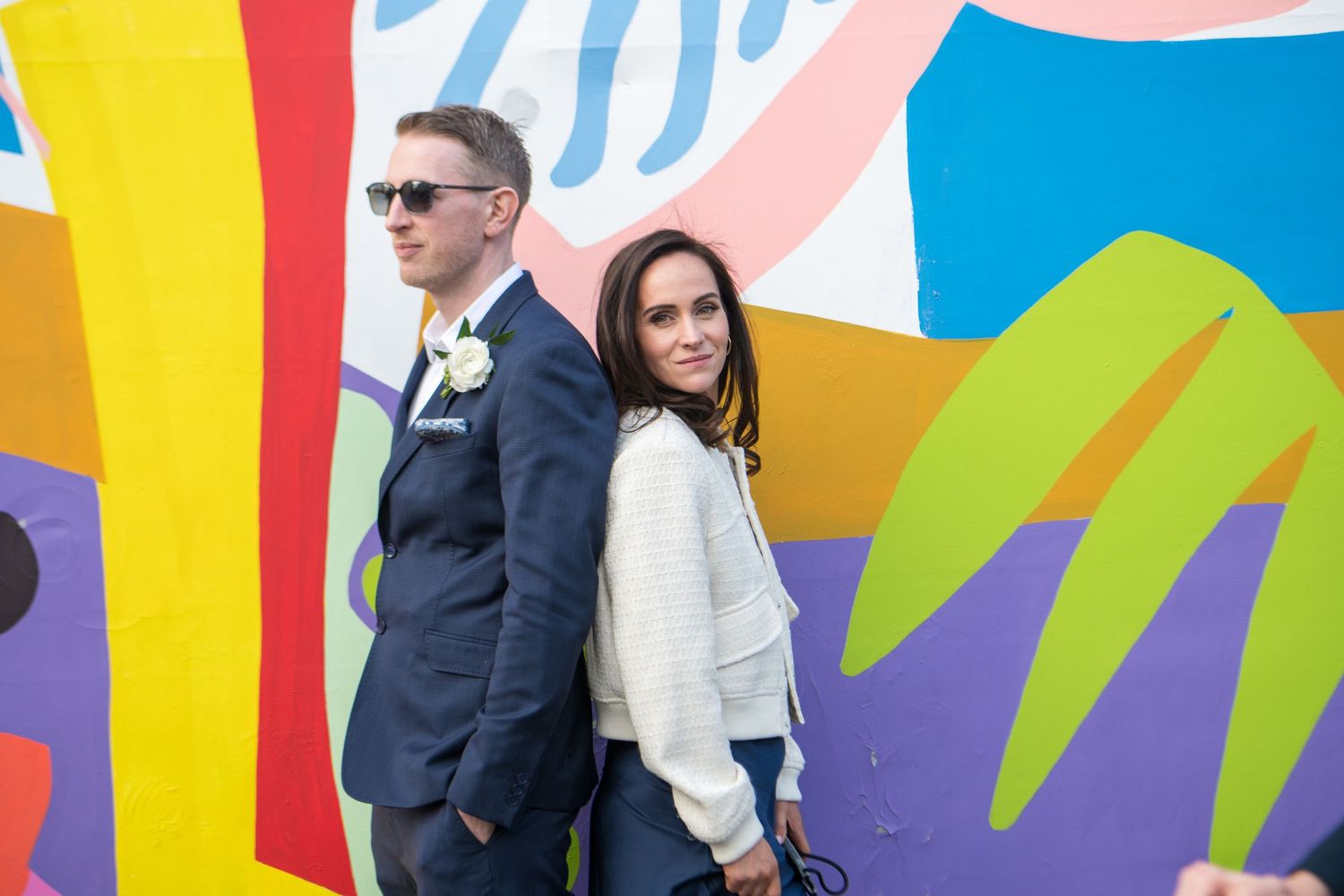 A stylish couple poses against a colorful abstract mural wall.
