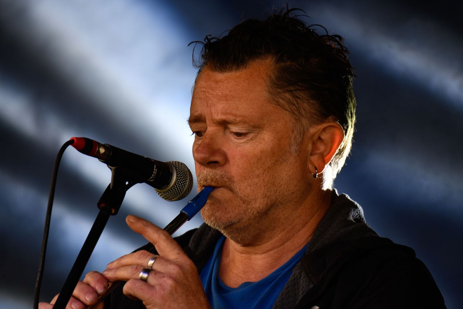 A performer sings passionately into a microphone with dramatic blue lighting in the background.