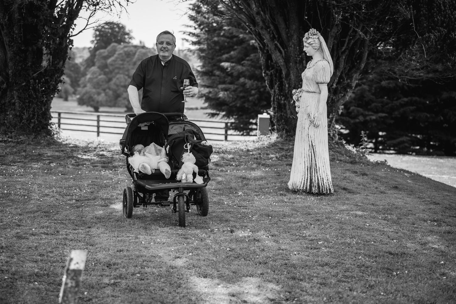 A black and white photo of a person pushing a stroller while another stands on a garden path.