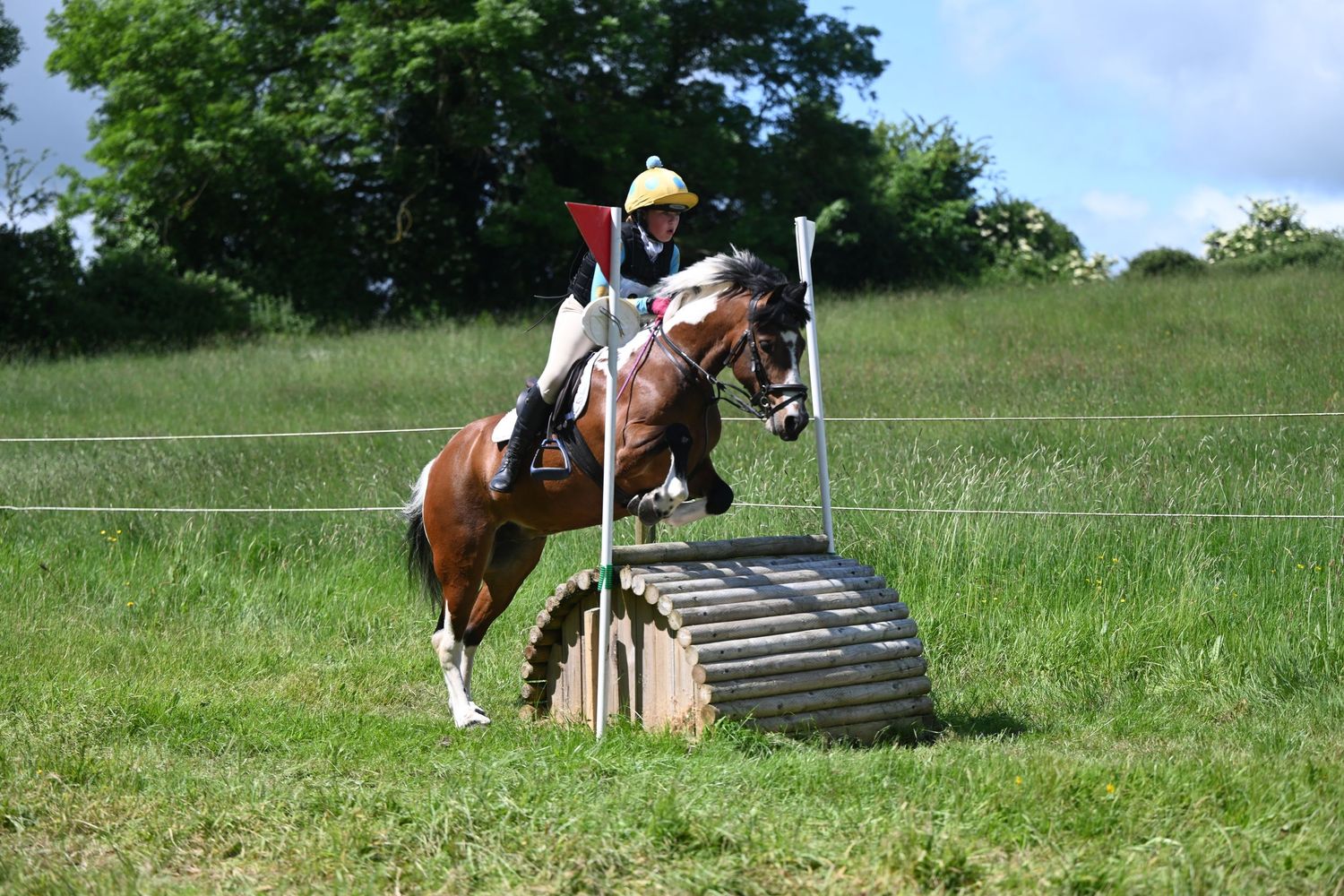 Horses and riders jumping over obstacles during a cross-country equestrian competition.