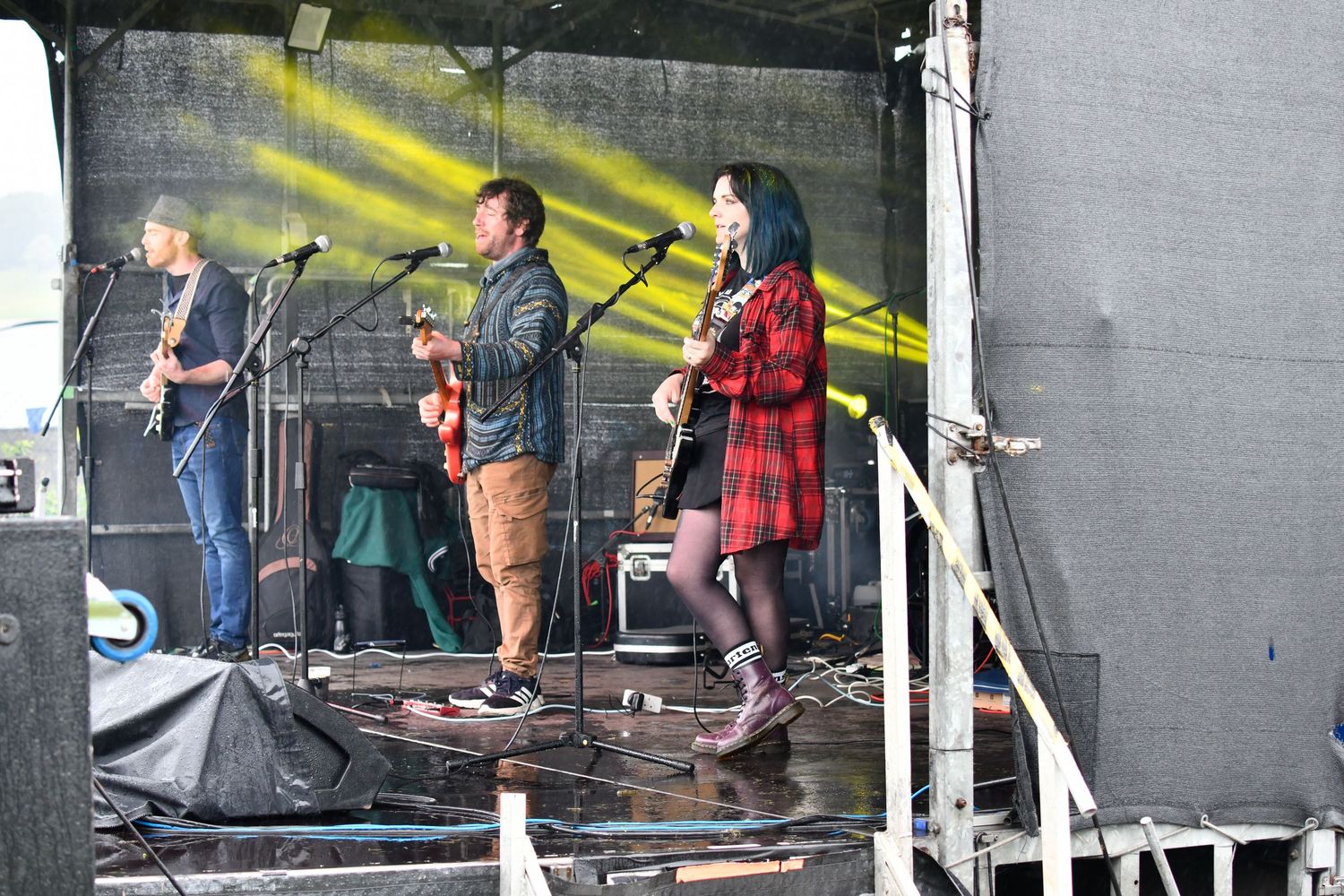 A band performs on an outdoor stage with dramatic yellow lighting and stage equipment.