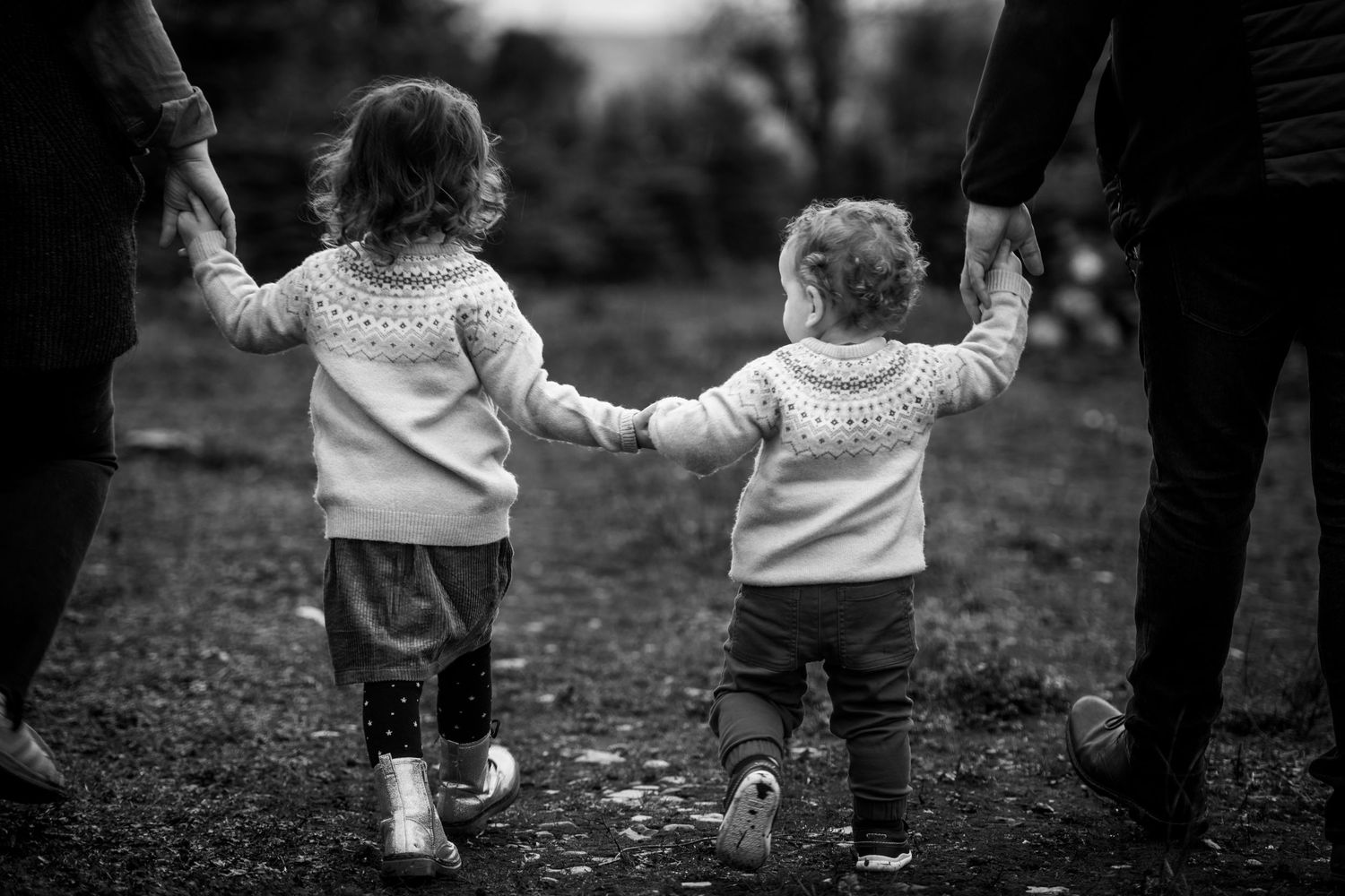 Black and white image of children walking hand in hand with adults on a nature path.