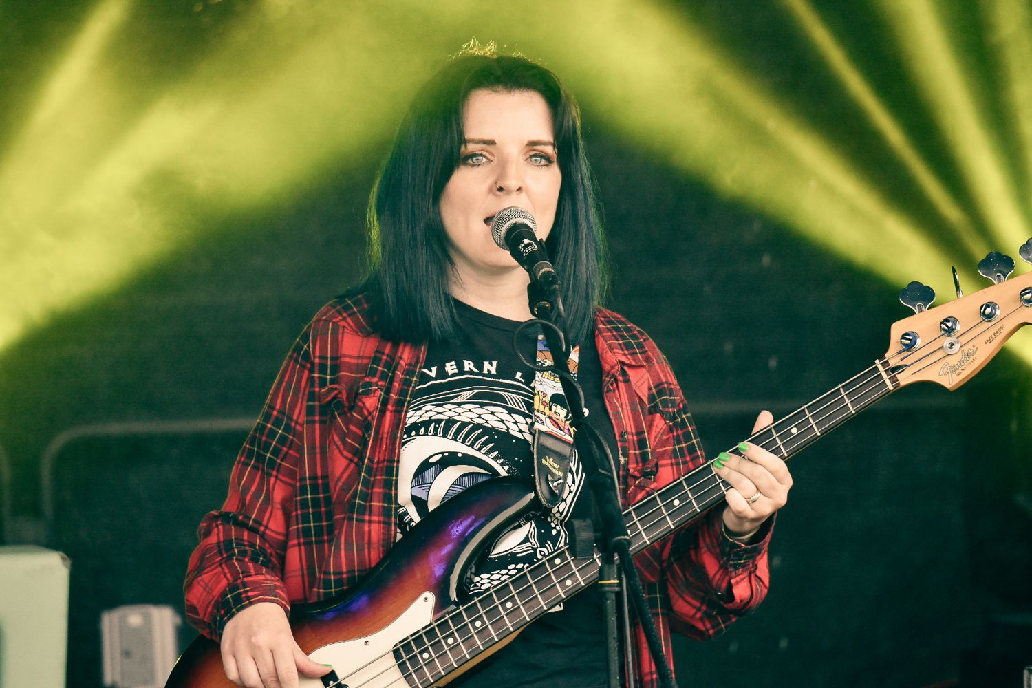 A bass player in a plaid shirt performs on stage with yellow lighting effects.