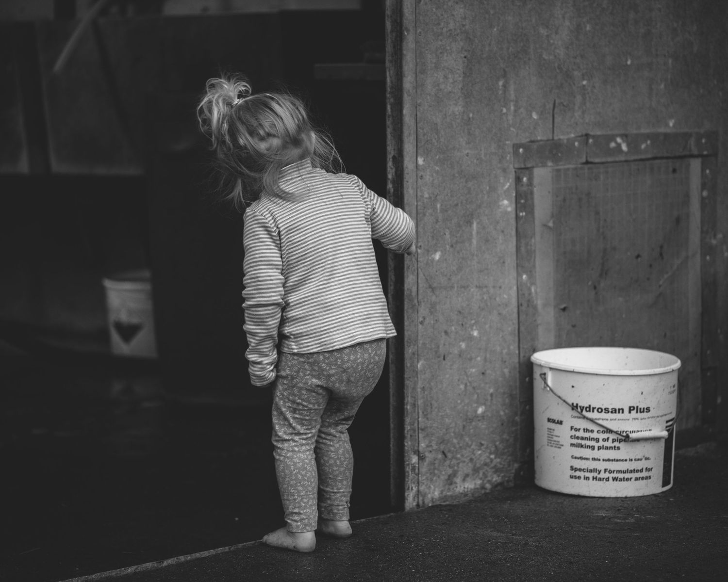 Small figure in sweater and patterned pants standing near a white bucket in a doorway.