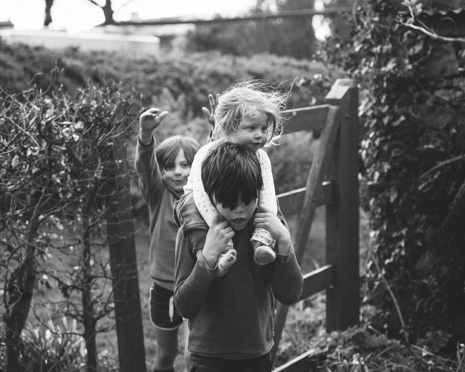 Black and white photograph showing childhood play on rustic wooden fence.