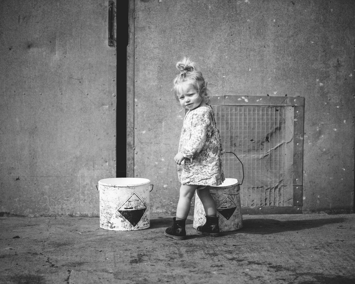 Small figure standing next to a white bucket against a concrete wall with a metal access panel.