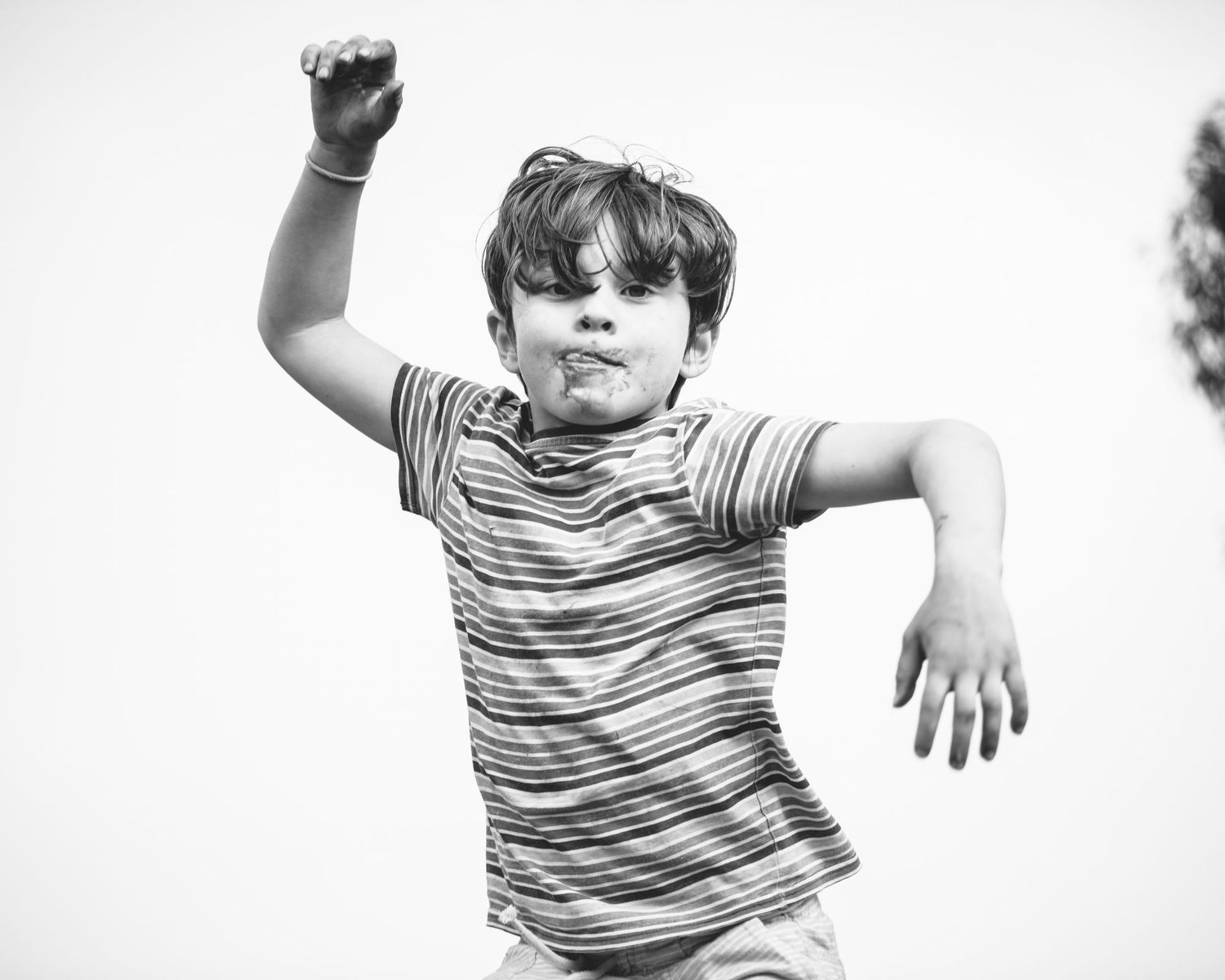 Child in striped shirt leaping joyfully against white background.