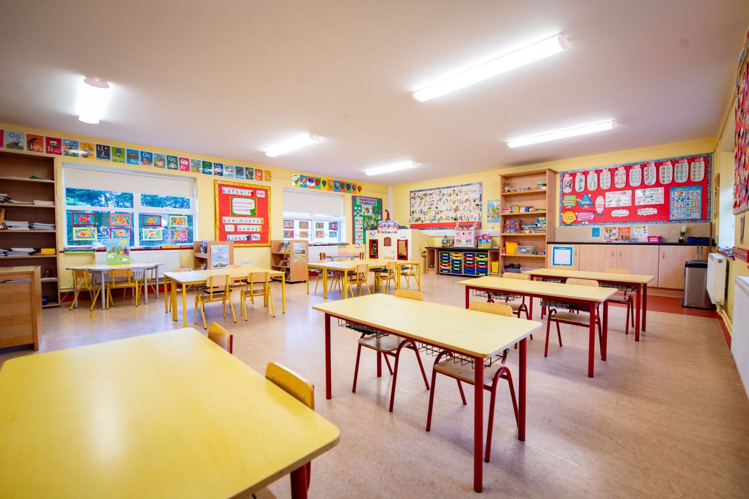 Empty classroom with rows of tables and colorful educational posters on yellow walls.