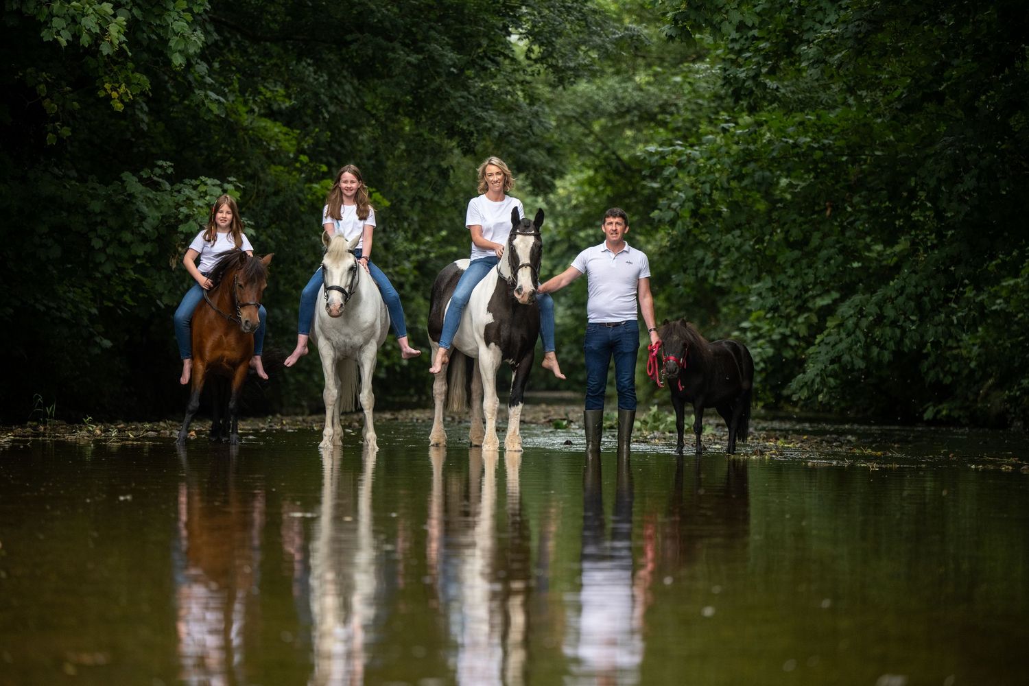 Group gathered around horses in a flooded field or water crossing.