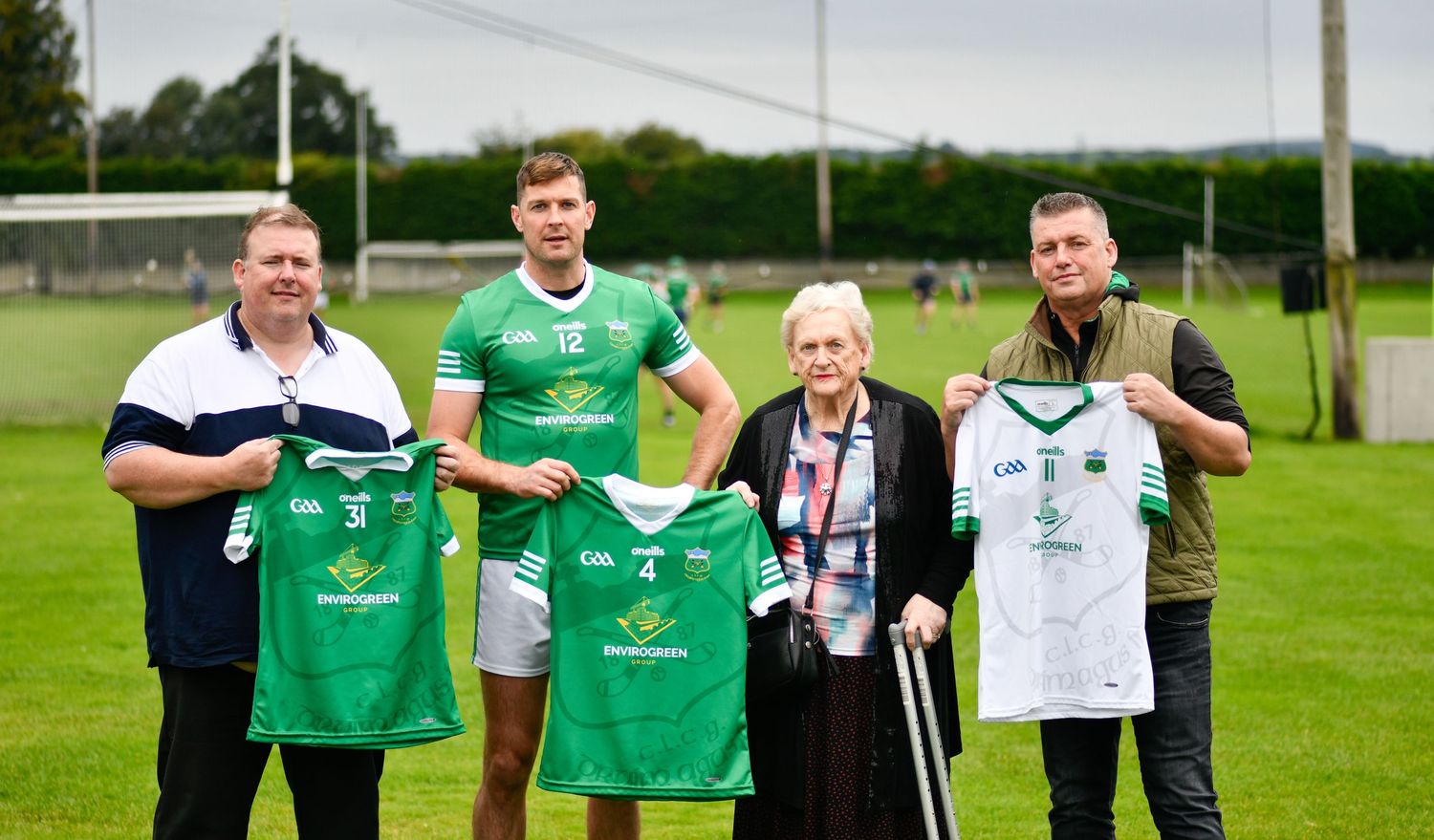 Sports team representatives display green and white jerseys at an outdoor presentation.