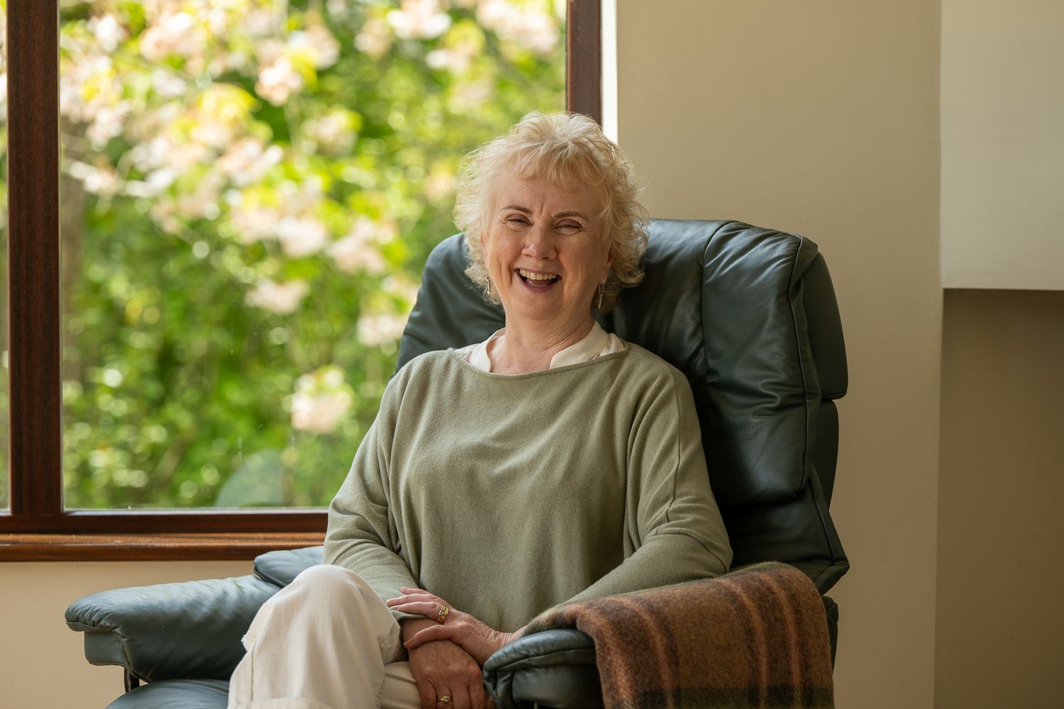 Senior person relaxing in green recliner chair near sunny window.