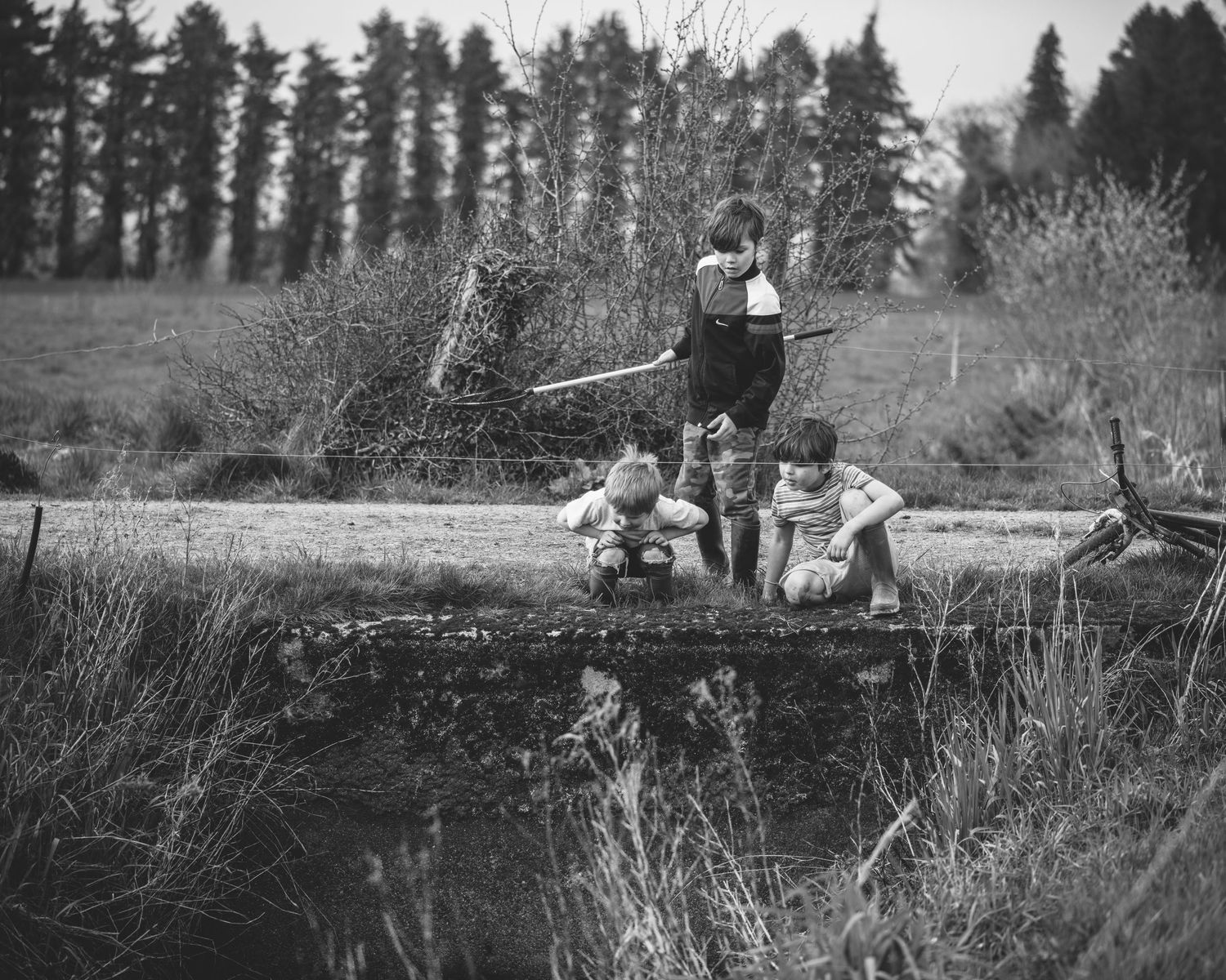 Vintage black and white photograph of children fishing together on a wooden bridge.